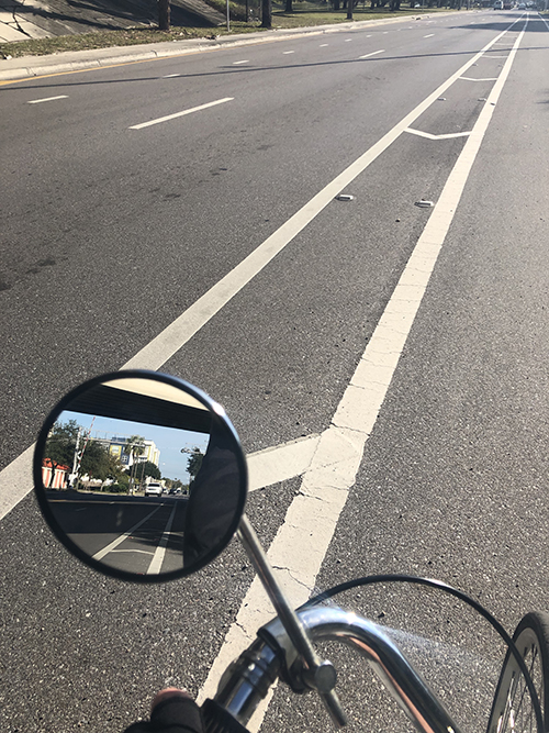 A wall of cars can be seen approaching in bicycle's rearview mirror.